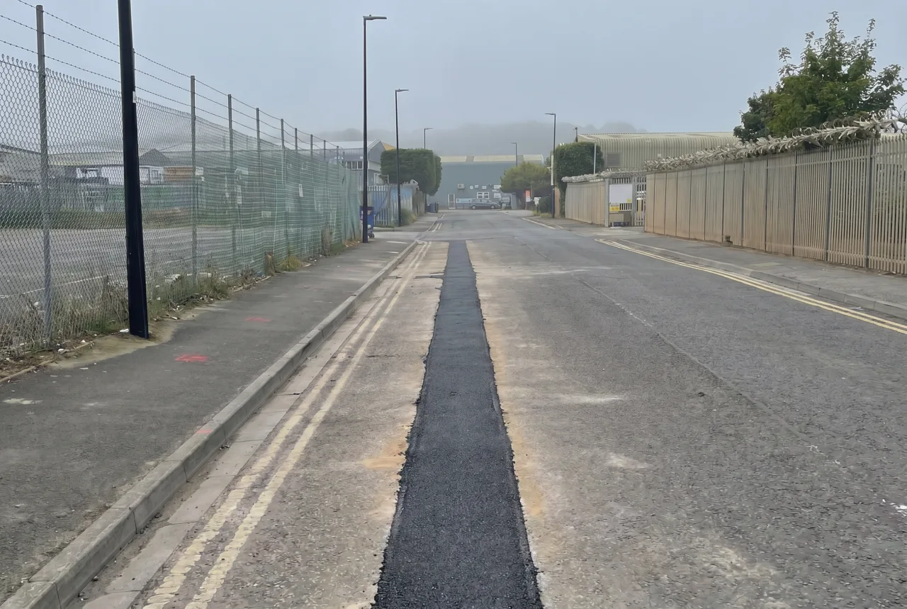 Completed disconnection and site clearance: a long fresh-tarmac reinstatement strip down a commercial estate road, the road made good