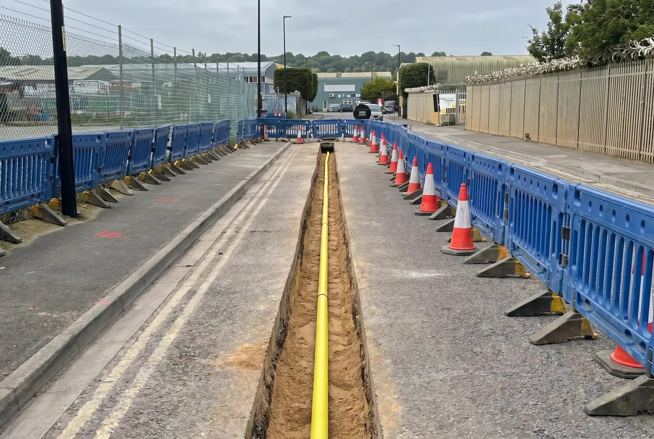 Completed gas connection project: a continuous yellow gas main in a clean trench lined with blue barriers on a commercial estate road